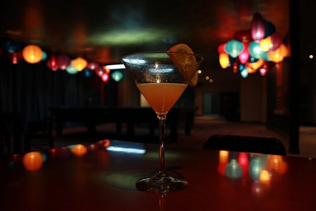 A cocktail glass on a dark bar with coloured lights blurred in the background.