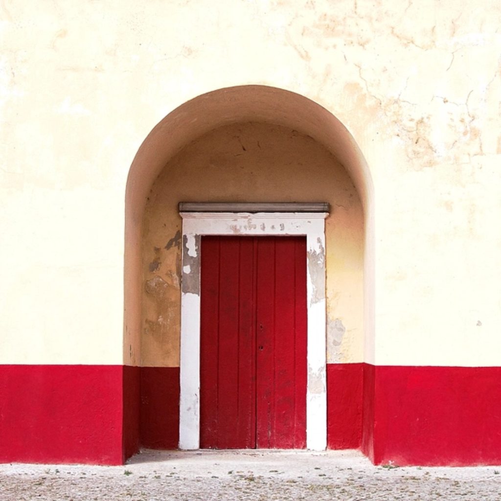 A tall arched doorway painted deep red, set into a pale rendered wall.