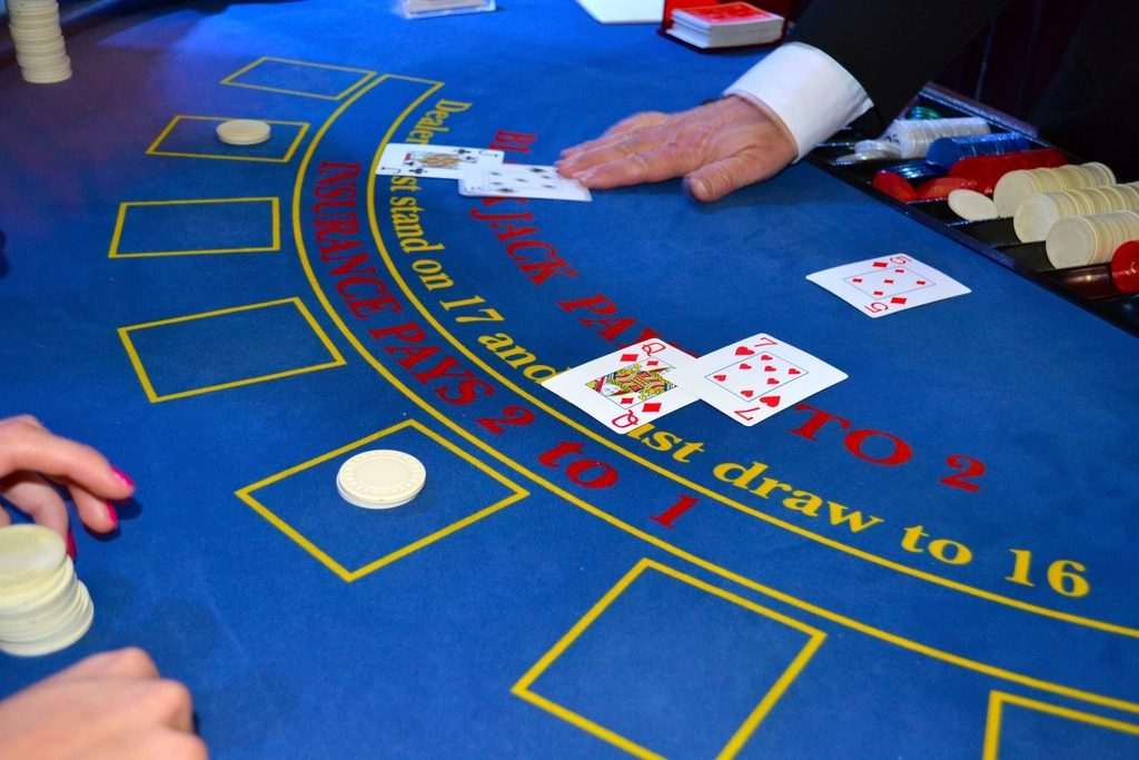 A dealer's hands placing playing cards and chips on a blue felt card table.