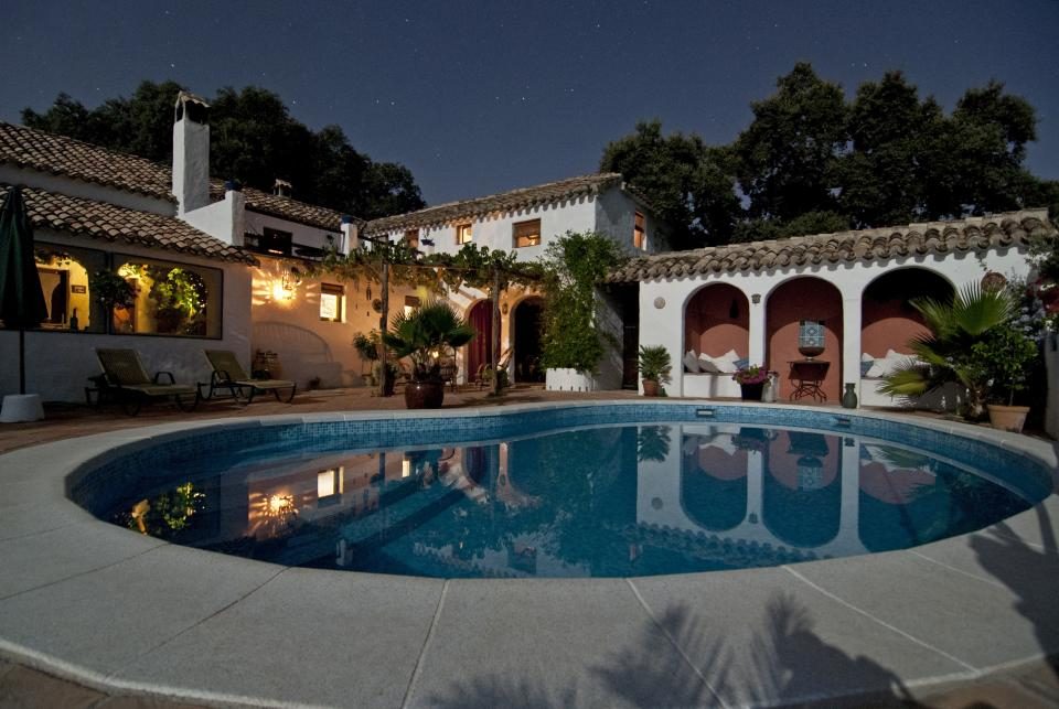 A white villa lit from within at dusk, arranged around its own curved swimming pool.