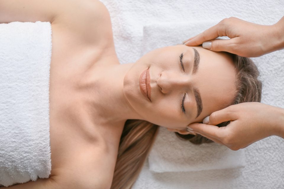 A person lying face up on a treatment table receiving a head and shoulder massage.