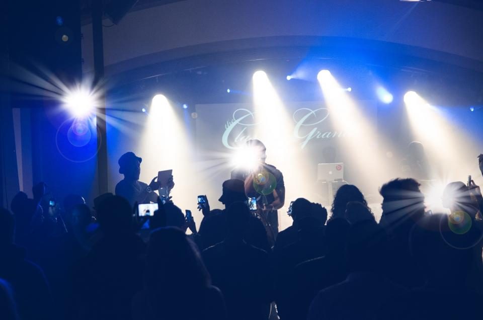 A concert stage seen over the heads of an audience, lit by beams of blue and white light.